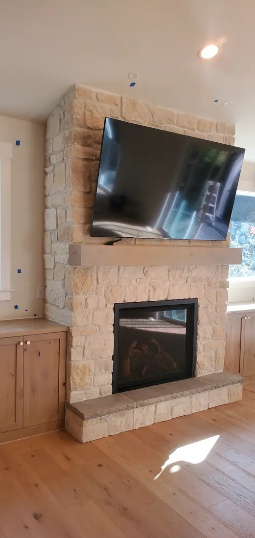 White stone veneer fireplace with mounted TV and wood beam mantel Oregon